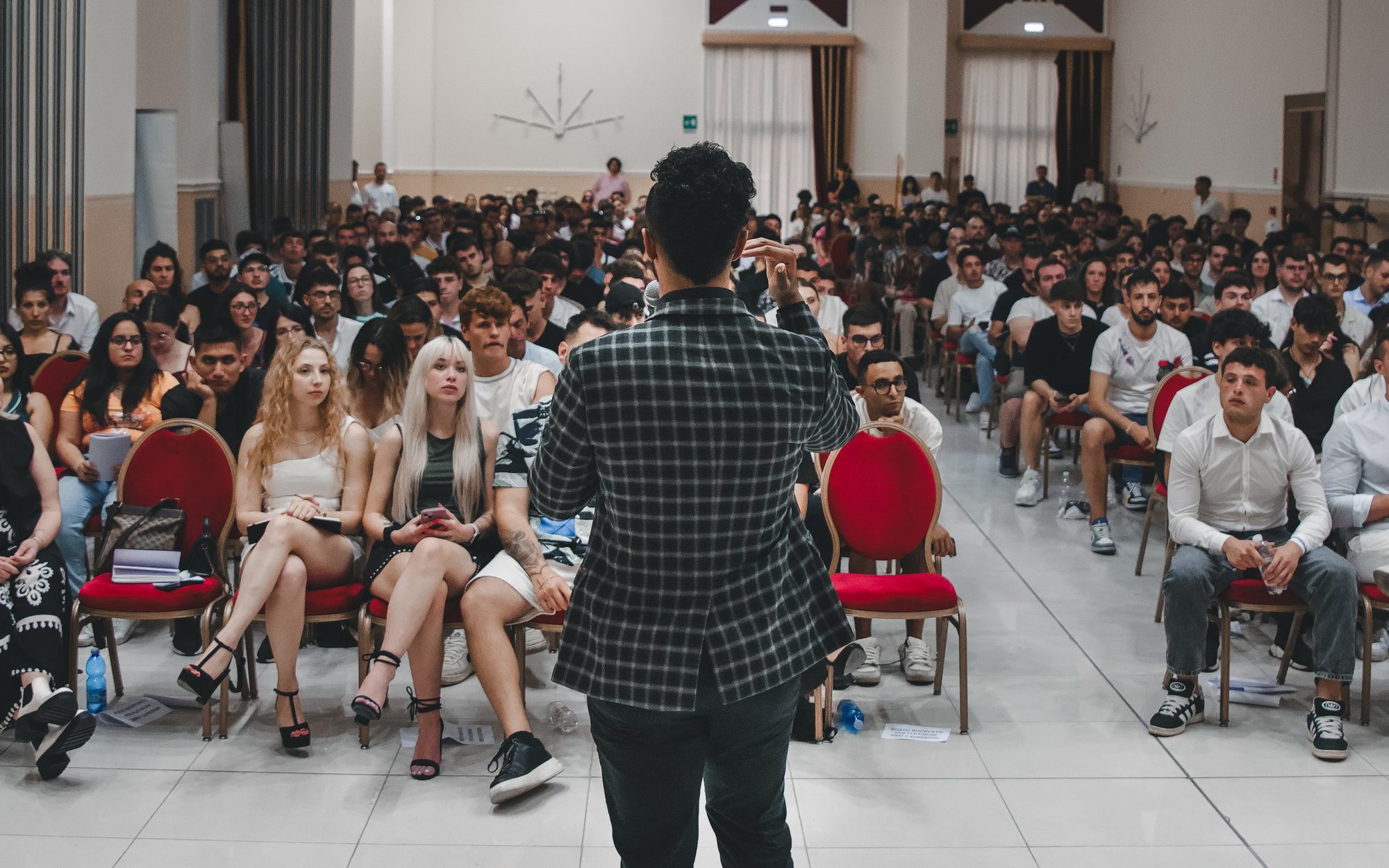 Neno speaking to a full room from the front, seen from behind